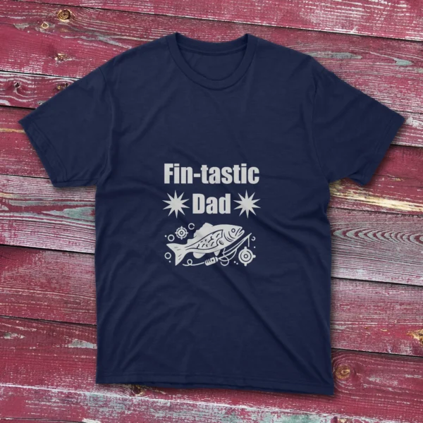 Navy blue T-shirt on a light red wooden ground featuring "Fin-Tastic Dad" with two stars and a decorative fish illustration in white.