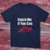 Navy fishing T-shirt featuring the phrase "Catch me if you can" in bold white text with a red fish illustration, set against a light blue background.