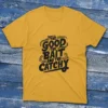 yellow T-shirt featuring the phrase "The Good, The Bait, And The Catchy" with bold fishing elements, displayed on a light blue background.